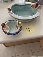 Photo of two whimsically designed ceramic bowls featuring figurines of swimmers integrated on the edges. The bowls sit on a white countertop.
