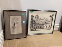 Two framed and matted art prints leaning against wall, showing size tags 20x15 and 21x26 respectively, frames with minor wear.