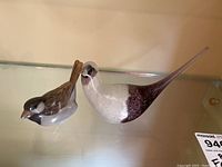 Both glass bird figures shown side by side on shelf, highlighting size and color contrast