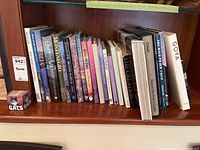 One shelf of assorted hardcover coffee table books, mostly non-fiction with colorful dust jackets and large formats, neatly arranged on a wooden shelf.
