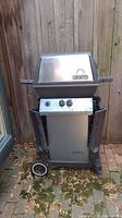 Front view of Broil King propane BBQ grill showing metal body, control knobs, wheels, and side shelves.
