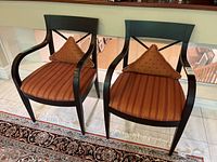 Pair of matching armchairs with dark wood frames and striped upholstered seats with two triangular orange throw cushions.
