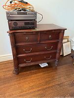 Full frontal view of four drawer dresser showing wood grain and decorative handles with electronics placed on top (contents not included).