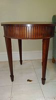 Side view of round wood end table showing slatted apron and tapered legs