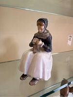 Photo of Royal Copenhagen porcelain figurine of seated lady knitting, showing front side with detailed features and clothing.