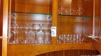 Glass cabinet displaying sets of clear glassware including red wine, cocktail, and snifter glasses