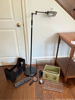 Front view of lot including adjustable black floor lamp, black file organizer, wire racks, hole punch, magnifying glass, silver bell, and decorative box with rooster images.