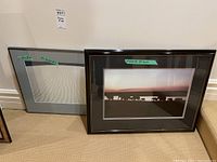 Two framed photo prints leaning against wall, one black frame with elephant silhouette photo, one gray frame with sand dune photo
