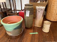 Photo showing large planter pot with plastic tray and three different pottery and ceramic vases on wooden floor.