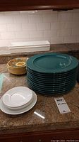 Plates stacked on a granite countertop showing turquoise large plates, patterned smaller plates and white plates in front.