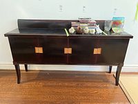 Front view of dark wood sideboard with items placed on top, showing two slide-out drawers and two cabinet doors with Asian writing.