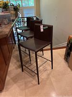 Three matching faux leather bar stools with metal frames placed in kitchen area, showing overall set and design.
