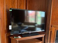 Sharp Aquos Quattron 46-inch flat screen TV front view on wooden corner TV stand in a corner of room with wood panel walls.