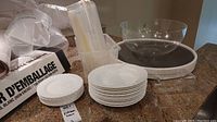 Overview of white Wedgwood bowls and plates stacked, clear plastic bowl, and food storage containers on counter