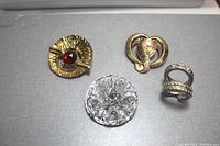 Four vintage scarf clips on a grey surface showing different styles and materials.