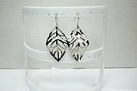 Pair of large silver-tone leaf earrings hanging on a white display stand shown from the front