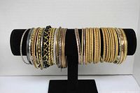 Front view of assorted gold, silver, and black bangle bracelets displayed on black stand.