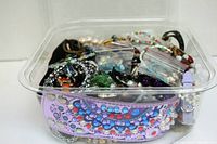 Clear containers filled with assorted bracelets showing variety of styles including studded leather cuffs, beaded strands, rhinestones and faux pearl bracelets.