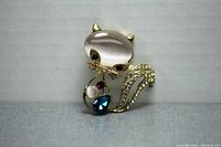 Front and angled side view of the gold tone kitty cat brooch showing translucent head stone, colored body stones, black eyes, and rhinestone decorated tail.