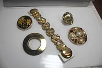 Image showing 4 vintage gold tone scarf clips and 1 gold tone sweater clip arranged on a white surface.