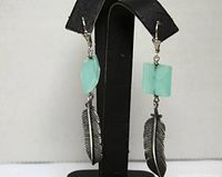 Front view of both earrings hanging on display stand showing feather pendants and aqua faceted stones