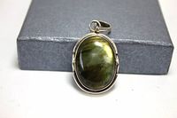Front view of a sterling silver pendant featuring a large oval cabochon greenish stone with a polished bezel setting and integrated bail.