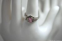 Ring on a white display hand showing the pink center stone and clear stones on each side.