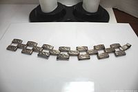 Full view of the silver bracelet showing all interconnected rectangular links with embossed swirl designs and bent clasp.