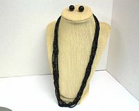 Front view of the vintage 6 strand black seed bead necklace displayed on a beige bust with matching black ball stud earrings pinned above.