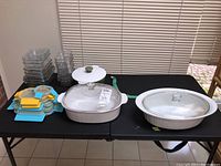 View of the full lot showing ceramic casserole dishes, glass storage containers, and colorful lids on a black table.