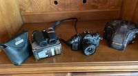 Photo showing the Canon A-1 camera body with attached FD 35mm f/2.8 lens, the Canon leather case on the right, and the Bausch & Lomb Legacy binoculars with their black case and original box on the left.
