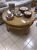 Full view of the round rattan coffee table with various dishes placed on top, showcasing the table's circular woven wicker surface and rattan frame.