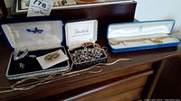 Overview of the costume jewelry including brooches, earrings, necklaces, and rosaries arranged on a wooden surface in boxes and loose.