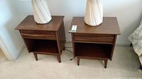 Pair of brown wooden night stands side by side each topped with a white table lamp