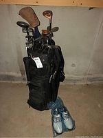 Full view of golf bag with clubs and golf shoes on basement floor.