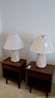 Full view of two ceramic table lamps on wooden tables with pleated lampshades
