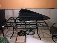 Photo showing the rectangular metal frame patio table with slots for tile inserts and a folded black umbrella resting on it, with a box of tiles underneath.