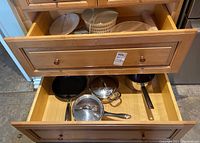Drawer showing three skillets and two pots with lids, including a pot with steamer insert