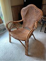 View of single rattan and cane high back chair with woven seat and intricate armrests