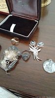 Assorted jewelry items laid out including rings, two floral brooches with stone details, and a pendant with religious motif.