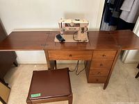 Wide shot showing sewing machine mounted in wooden table with side leaves extended and matching padded stool.