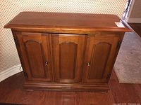 Front view of the wood side table with three doors showing overall wear and finish condition.