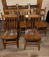 Group photo of all eight antique wooden press back chairs showing their matching finish and design.