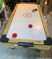 Overall front view of the air hockey table showing the playing surface with four mallets and the score keeper.