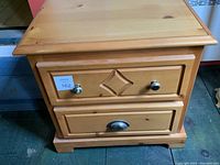 Front view of wooden bedside table showing two drawers, metal handles, and diamond carved detail on top drawer.