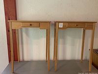 Front view of the two matching wooden bedside tables with drawers, showing tapered legs and drawer knobs