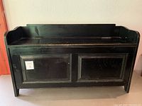 Front view of black wooden storage bench with paneled front, showing overall structure and design.