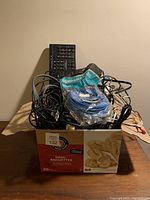 Box filled with mixed cables, blue Ethernet cable in package, old style keyboard visible behind cables