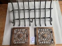 Photo showing one metal fireplace grate and two copper floor grates with intricate cutout designs.