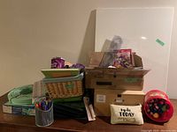 Overview of assorted craft supplies including boxes, basket, papers, cups of pens, and a motivational pouch